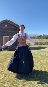 Video stillbilde av kvinnebunad fra Østerdalen i rød brokade vest og sort stakk.