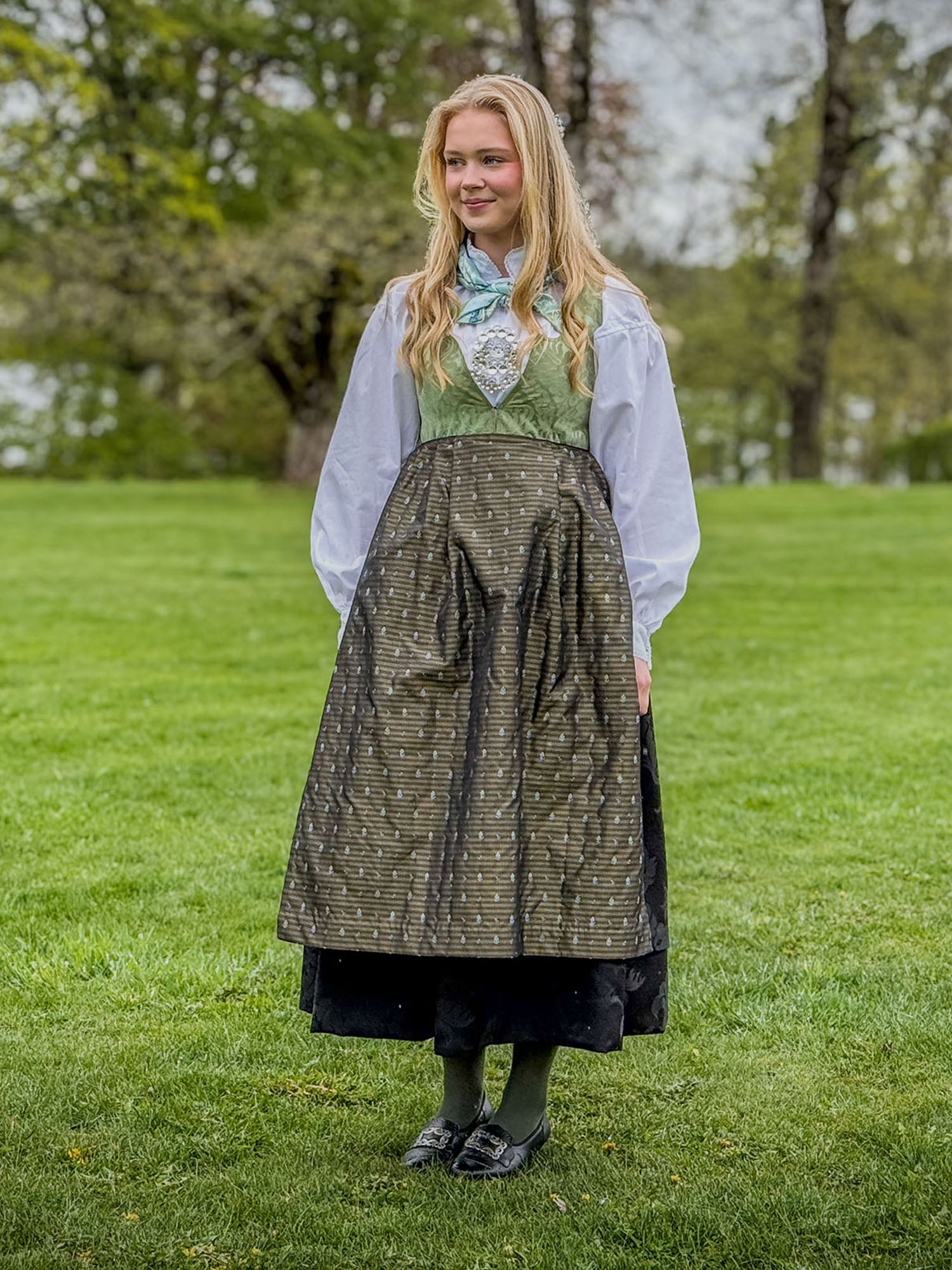 Jente i damaskkjol med grønt liv, sort stakk og grønt silkeforkle ute på Bogstad Gård