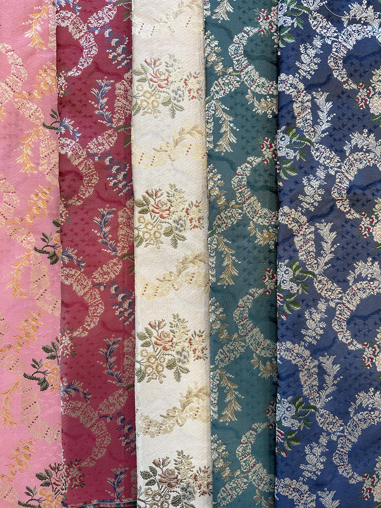 5 ulike farger av silkestoff av typen Dauphin Lampas silkebrokade bunadsstoff: Rosa, Rød, Creme, Grønn og Blå. Bestilles som metervare i nettbutikken